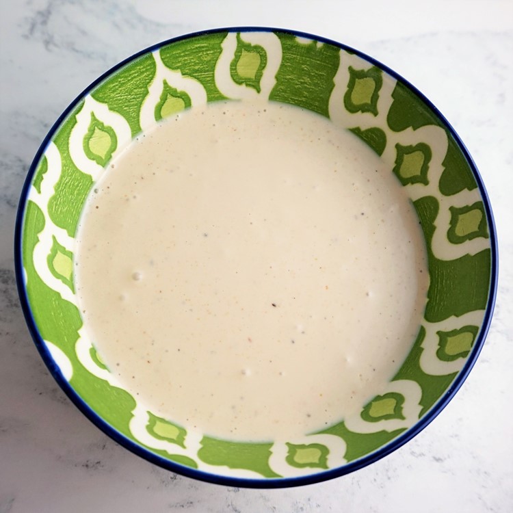 a green patterned bowl with caesar salad dressing inside