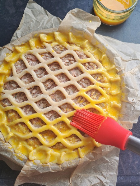 glazing Sausage & Onion Lattice Pie with beaten egg